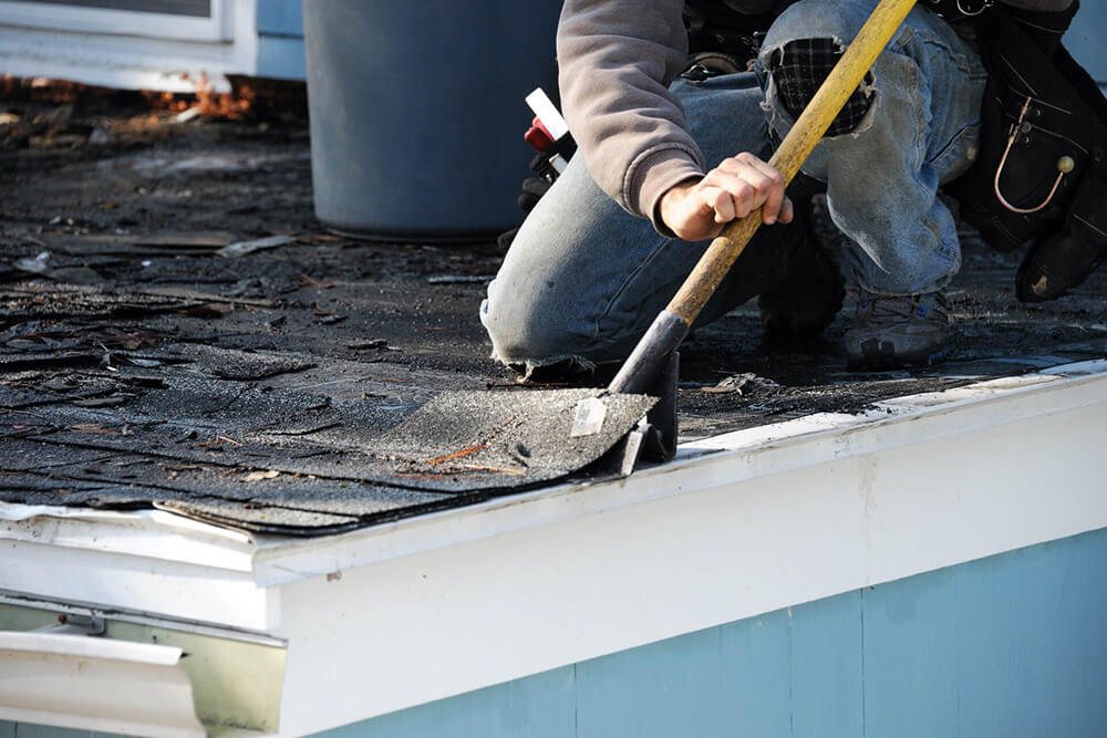 a roofer removing damaged shingles on a house